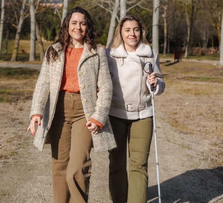 Freizeitgestaltung im Park Frau mit Blindenstock läuft eingehackt am Arm einer anderen Frau im Park